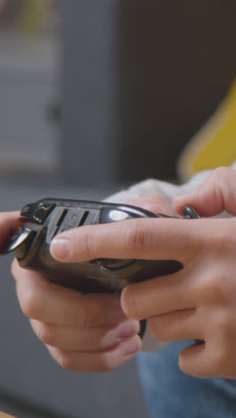 Vertical-Video-Close-Up-Of-Woman-Holding-Controller-Sitting-On-Sofa-At-Home-Gaming-Online-